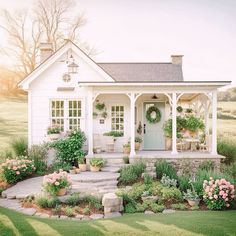 a small white house with lots of flowers and plants around the front door is shown