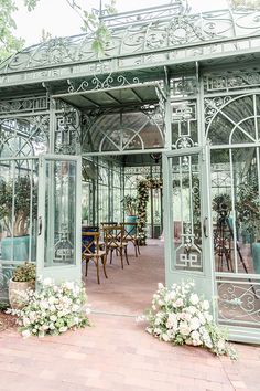 an ornately decorated glass building with flowers in the foreground and tables on either side