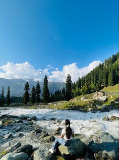 a woman sitting on top of a rock next to a river