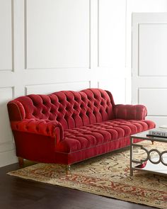 a red couch sitting on top of a wooden floor next to a glass coffee table