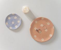 two wedding rings are sitting on a plate next to a flower ring dish that is shaped like a button