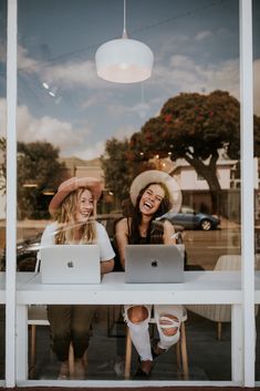 two women sitting at a table in front of a window with their laptops open