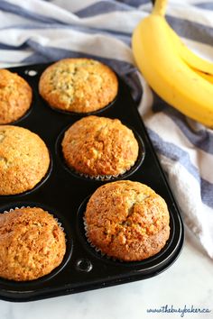 banana muffins sitting in a black tray next to a ripe banana on a blue and white towel