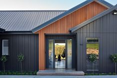 the front entrance to a modern home with wood siding and metal roofing, along with potted plants on either side