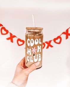 a hand holding a mason jar with the words cool mom club on it and a straw