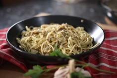 a black bowl filled with pasta on top of a red and white checkered table cloth