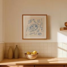 a bowl of lemons sits on a counter in front of a framed artwork above it