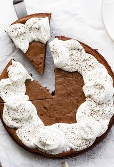 a chocolate cake with whipped cream on top and one slice missing from it, sitting on a white plate