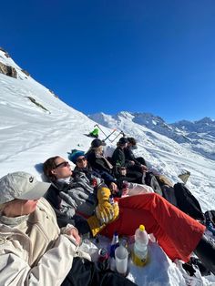 a group of people sitting on the side of a snow covered slope next to each other