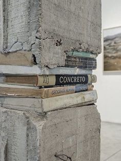 a stack of books sitting on top of a cement pillar in an art gallery next to paintings