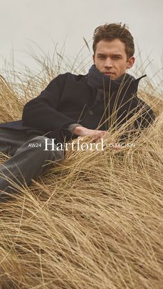 a man sitting on top of a tall grass covered field with his hand in his mouth