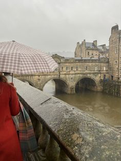 a woman with an umbrella standing on a bridge over looking the water and old buildings