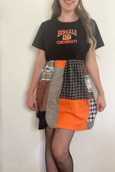 a woman standing in front of a wall wearing an orange skirt and black t - shirt