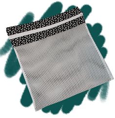 a white mesh bag with black and white designs on the front, sitting on top of a green background