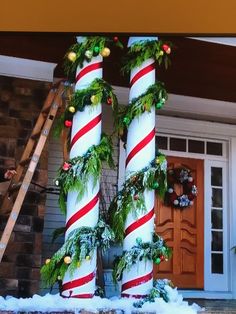 two giant candy canes decorated with greenery and christmas lights in front of a house