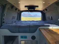 the interior of a camper with a bed and desk in front of an open window