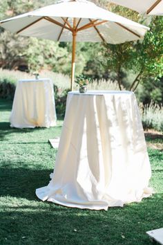 an umbrella and table set up on the grass for a wedding reception in front of some trees