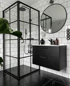 a black and white tiled bathroom with a shower, sink, mirror and plant in the corner