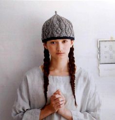 a woman with long braids wearing a knitted hat and standing in front of a wall