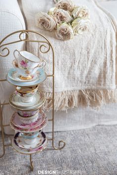 a stack of tea cups and saucers on a stand in front of a bed