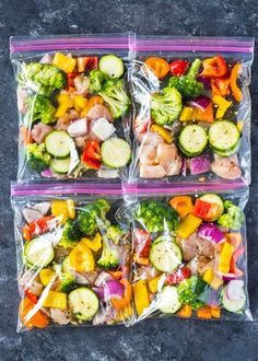 three plastic bags filled with assorted veggies on top of a gray surface