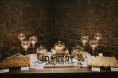 a table topped with lots of cookies and desserts next to wine glasses on top of a stone wall