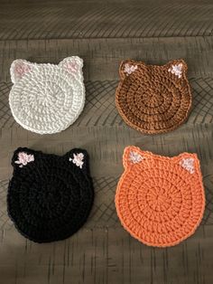 four crocheted cat coasters sitting on top of a wooden floor