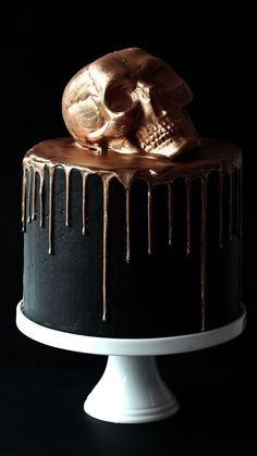 a black and gold decorated cake with a skull on it's top, drizzled in icing