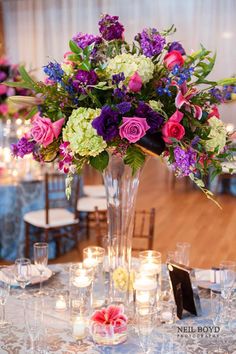 a tall vase filled with lots of purple and white flowers sitting on top of a table