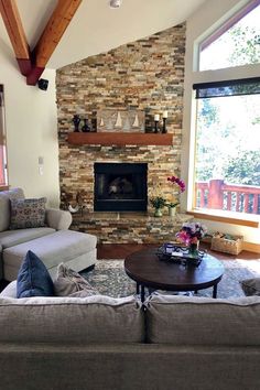 a living room with two couches and a fireplace in the corner, surrounded by windows