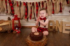 a baby boy sitting on the floor in front of a cake with red and black decorations