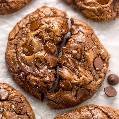 chocolate chip cookies on top of white paper with chocolate chips around them and one cookie broken in half