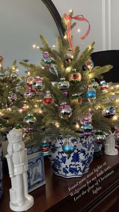 a small christmas tree in a blue and white pot on a table with other ornaments