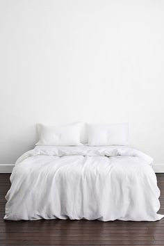 a bed with white sheets and pillows on top of it in front of a wall