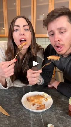 two people sitting at a table with food in front of them and one person holding a spoon