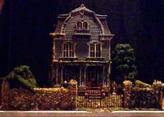 a doll house on display in front of a black wall with trees and bushes around it