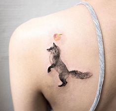 the back of a woman's shoulder with a tattoo of a fox and an apple