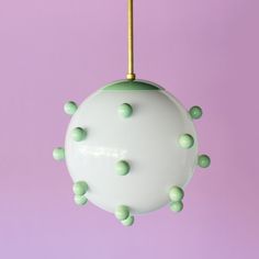 a green and white ball hanging from a gold colored hook on a purple background with tiny dots