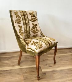 an upholstered chair sitting on top of a hard wood floor next to a wall