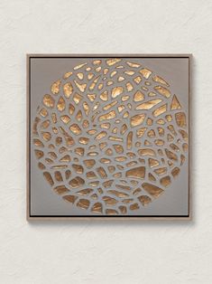 a square metal artwork with gold foil on the bottom and silver background, in front of a white wall