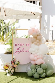 a baby in bloom sign surrounded by balloons and greenery on the lawn with flowers