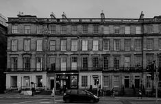 a black and white photo of an old building with cars parked in front of it