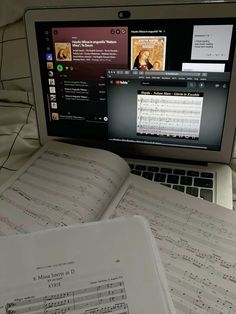 an open book sitting on top of a laptop computer next to music sheets and sheet music