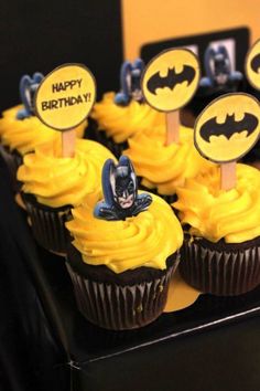 cupcakes decorated with yellow frosting and batman stickers are displayed on a table