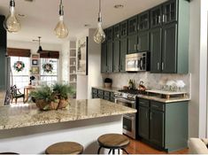 a kitchen with green cabinets and marble counter tops, hanging lights over the stove top