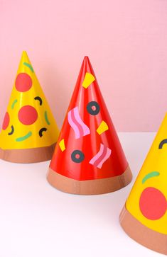 three party hats with different designs on them sitting on a white countertop against a pink wall