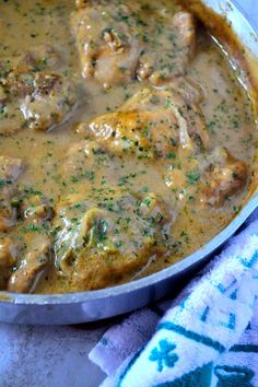 a pan filled with meat and gravy on top of a blue table cloth