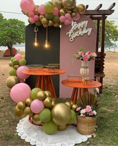 a table with some balloons on it in front of a pink and gold sign that says happy birthday