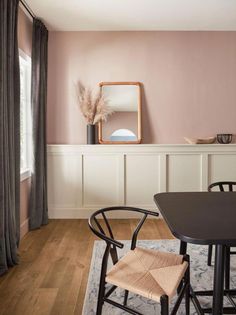 a dining room with pink walls and black chairs in front of a mirror on the wall