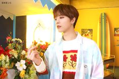 a young man standing next to a vase filled with flowers and holding something in his hand